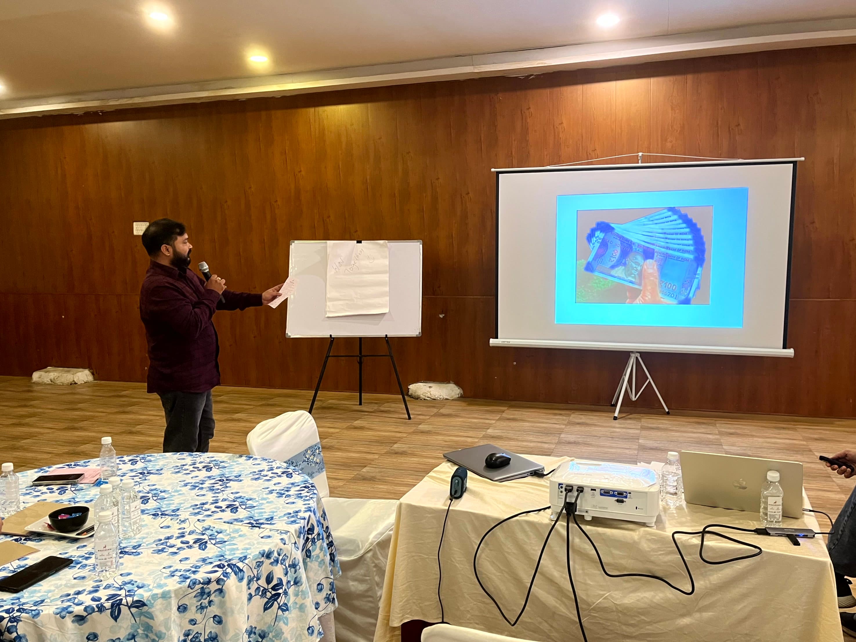 A FusionFoundry team member presenting at a whiteboard beside a projector screen during a workshop session